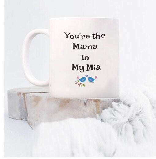 White mug with "You're the Mama to My Mia" and two blue birds, displayed on a marble stand for gift product.